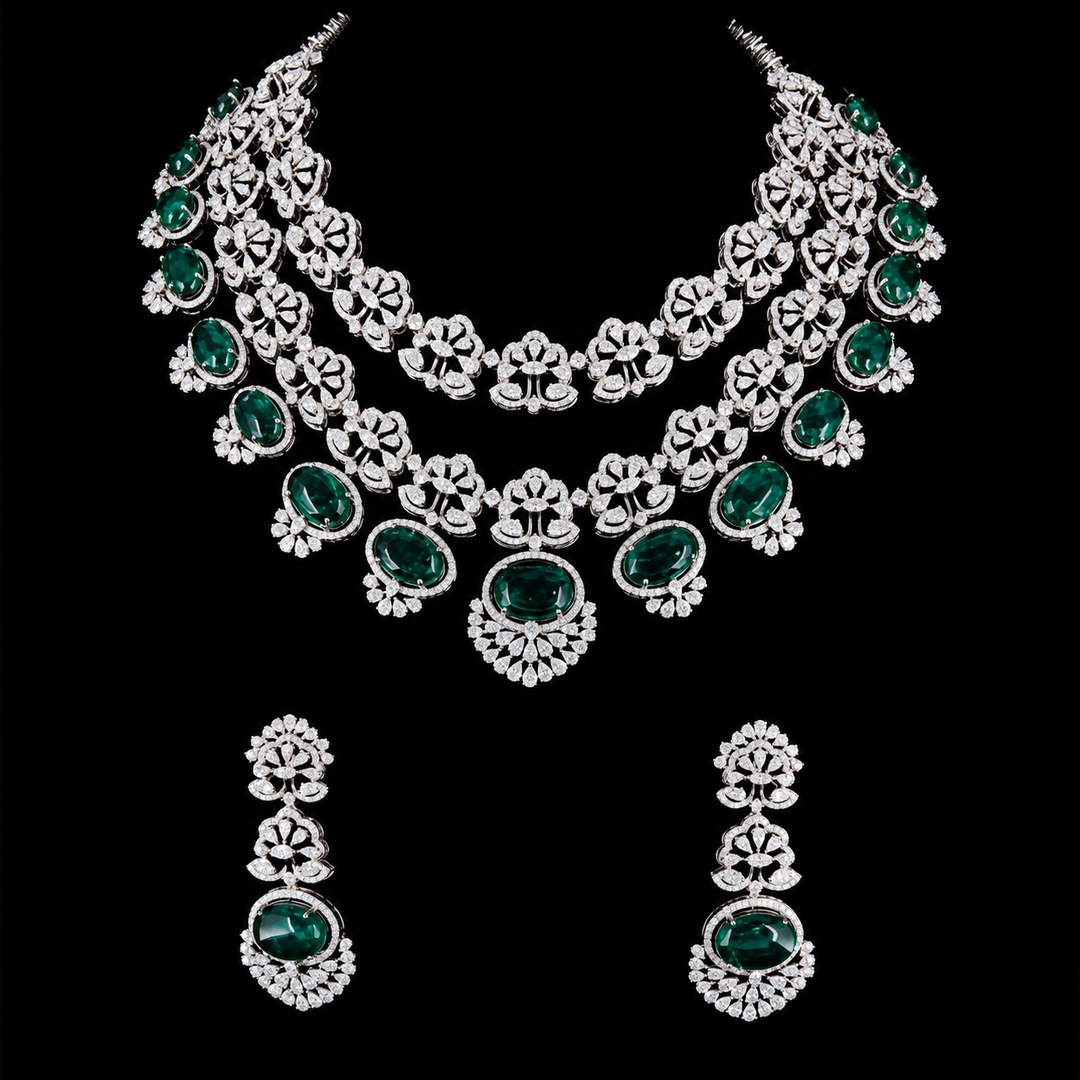 A silver-tone jewelry set featuring a multi-strand statement necklace and matching drop earrings, both adorned with oval green emerald-cut gemstones and surrounding clear stones, displayed against a solid black background.