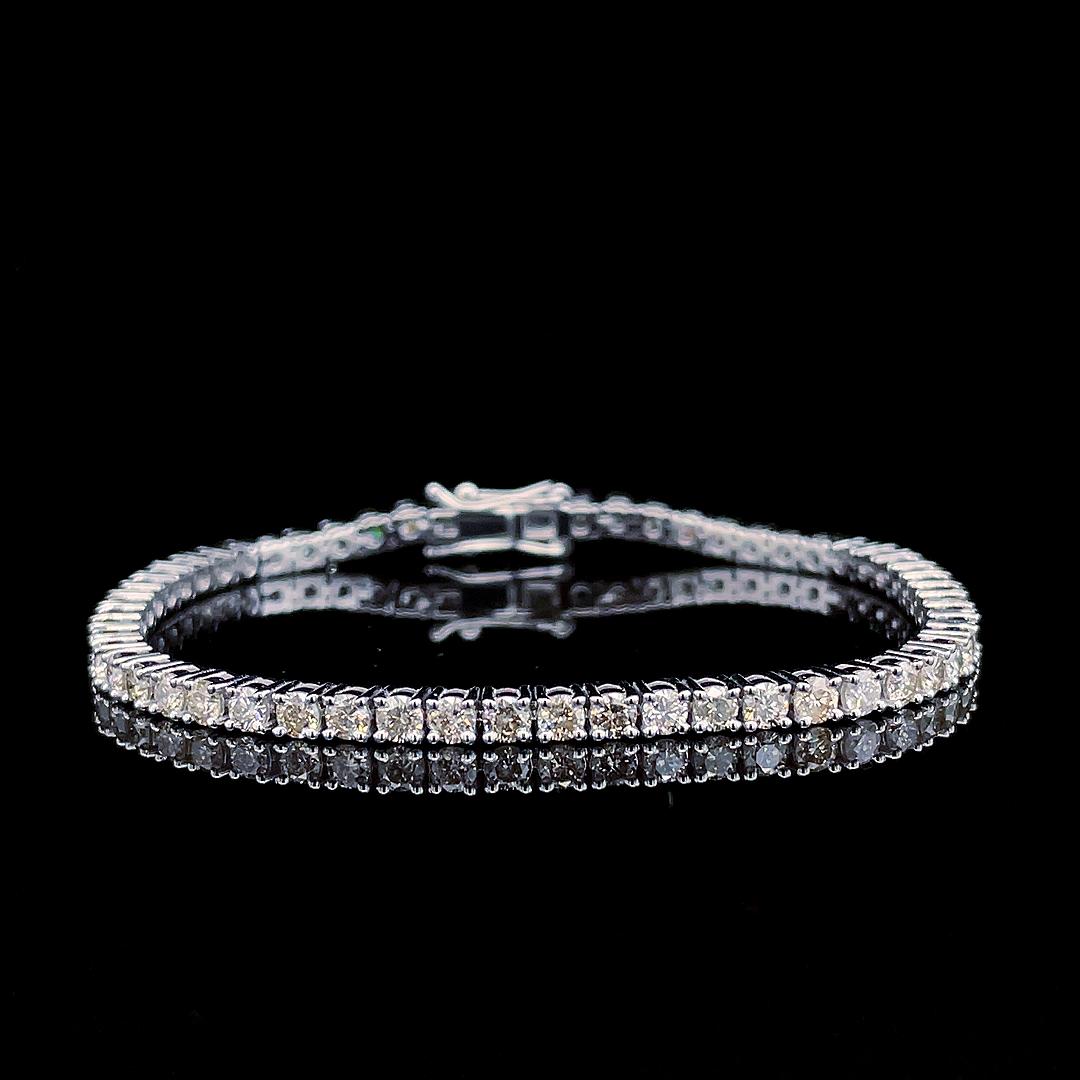 A single-row diamond tennis bracelet in silver-toned metal, displayed on a reflective black surface against a solid black background.